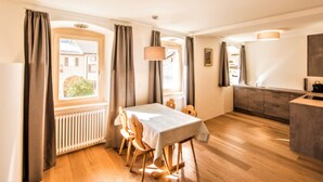 Ein Essbereich mit Tisch und Stühlen, eine Küche mit Arbeitsplatte und Schränken sowie ein Fenster mit Vorhängen.