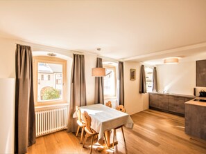 Ein Essbereich mit Tisch und Stühlen, eine Küche mit Arbeitsplatte und Schränken sowie ein Fenster mit Vorhängen.
