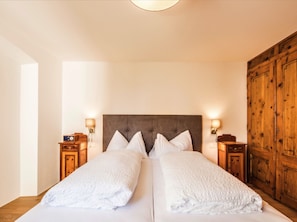 Een tweepersoonsbed met witte lakens, een houten kledingkast en twee nachtkastjes met lampen.