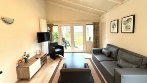 A spacious living area with a sofa, a coffee table, a TV, and a sliding glass door leading to a balcony. - Bungalowpark Simpelveld - Schakel 6 by Interhome (Simpelveld)