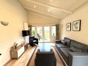 Un vaste espace de vie comprenant un canapé, une table basse, un téléviseur et une porte-fenêtre coulissante donnant sur un balcon.