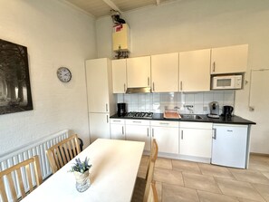 A compact kitchen with white cabinets, a microwave, a stove, and a sink. There's a clock on the wall and a small potted plant on the table. - Bungalowpark Simpelveld - Schakel 6 by Interhome (Simpelveld)