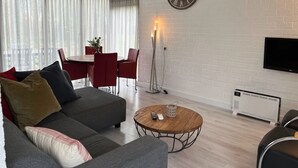 Una sala moderna con un sofá, una mesa redonda de centro, un comedor con sillas, un reloj de pared y un televisor de pantalla plana.