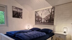 Un dormitorio con cama blanca, ropa de cama azul, una mesita de noche y dos lámparas de pared.