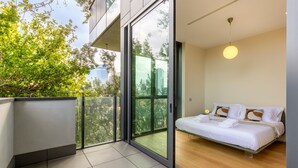 A modern bedroom with a large window, a bed, and a balcony with a view of trees and buildings. - Unique Bosco Verticale Apartment: Live in the World's Icon (Milano)