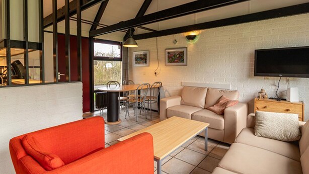 A modern living room with a high ceiling, a dining area, and a television mounted on the wall. - Bungalowpark Simpelveld - Alpha 79 by Interhome (Simpelveld)