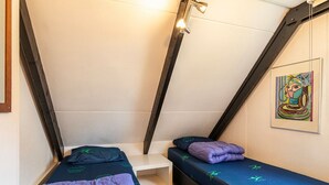 A small, triangular room with two beds, a white shelf, and a painting on the wall. - Bungalowpark Simpelveld - Alpha 79 by Interhome (Simpelveld)