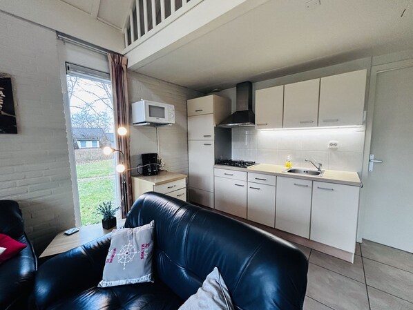 Ein gemütlicher Wohnbereich mit Küchenzeile, einem Ledersofa und einem Fenster mit Vorhängen.