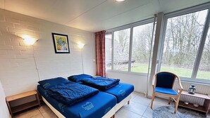 Ein Zimmer mit einem Bett, einem Sessel, einem Fenster und einem Bild an der Wand.