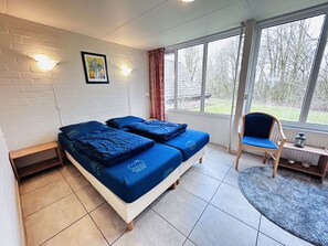 Ein Zimmer mit einem Bett, einem Sessel, einem Fenster und einem Bild an der Wand.