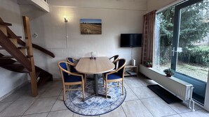 Ein Essbereich mit einem runden Tisch, blauen Stühlen, einer Holztreppe, einem Fernseher und einem Fenster mit Blick auf Bäume.
