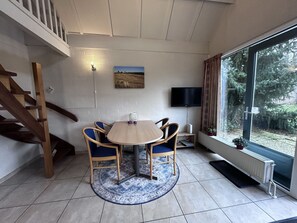 Ein Essbereich mit einem runden Tisch, blauen Stühlen, einer Holztreppe, einem Fernseher und einem Fenster mit Blick auf Bäume.