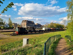Ein Bahnhof mit einem stehenden Zug, Gleisen und einem Gebäude im Hintergrund.