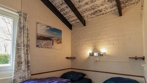 Ein Zimmer mit zwei Betten, einem Fenster mit Vorhängen, einer Ziegelwand und einem Gemälde.