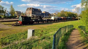 Ein Bahnhof mit einem stehenden Zug, Gleisen und einem Gebäude im Hintergrund.