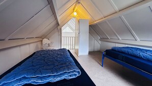 Ein kleines Schlafzimmer im Dachgeschoss, mit schrägverdeckter Decke, einem Bett, einem Sessel und einem Fenster.