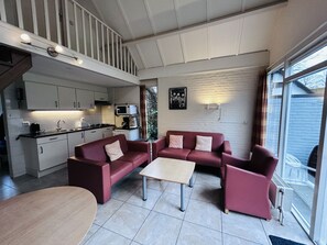 A compact living space with a kitchenette, a sofa set, a coffee table, and a view through a glass door. - Bungalowpark Simpelveld - Delta 154 by Interhome (Simpelveld)