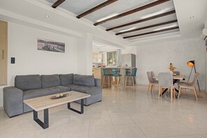 Een moderne woonkamer met een grijze modulaire bank, een houten salontafel en een eethoek met een tafel en stoelen.