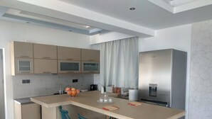 Cuina moderna amb una illa central, tamborets de bar, nevera d'acer inoxidable i un dispensador d'aigua.