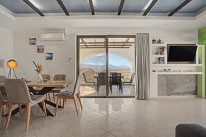 A modern living room with a dining area, a TV, and a view of the mountains. - Villa 'Gusta' with Sea View, Wi-Fi and Air Conditioning (Thólos)