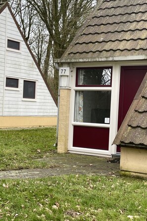 A small house with a red door and a window, number 77, with a paved entrance and a grassy yard. - Bungalowpark Simpelveld - Alpha 77 by Interhome (Simpelveld)