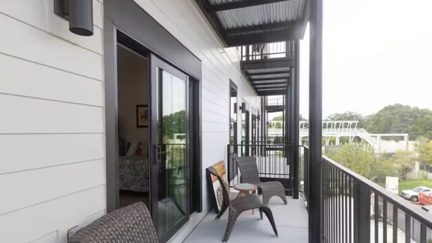 A balcony with wicker chairs, a small table, and a glass door leading to an interior room. - Gorgeous Old Town Bay St Louis Luxury Studio condominium! (Bay St. Louis)