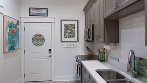 A kitchen with a white door, stainless steel appliances, and a double sink. - Gorgeous Old Town Bay St Louis Luxury Studio condominium! (Bay St. Louis)