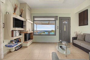 Una sala de estar con televisor, libros, chimenea, una mesa de centro de vidrio y vista al mar.