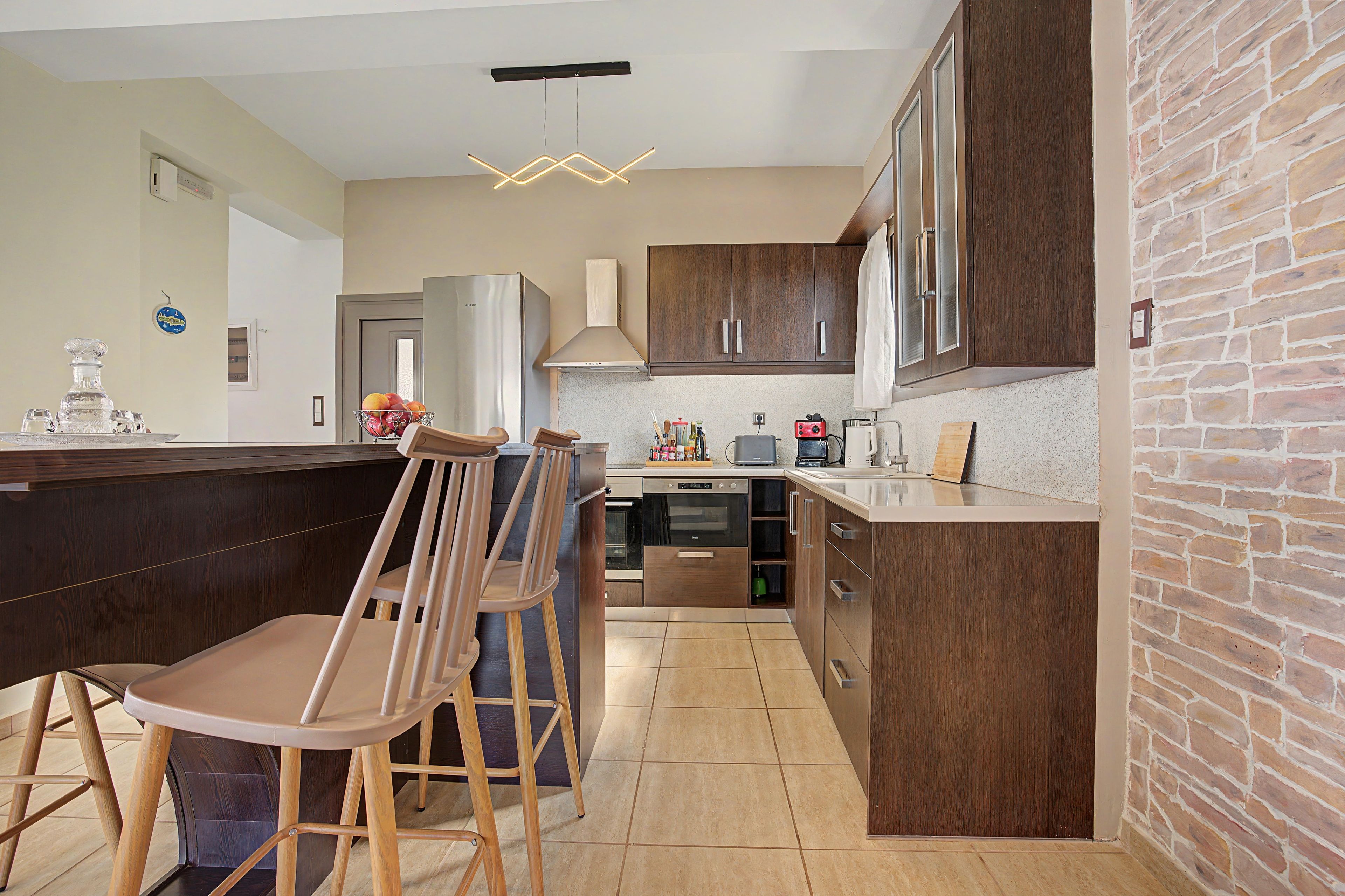 A modern kitchen with a central island, bar stools, a built-in oven, and a brick accent wall.