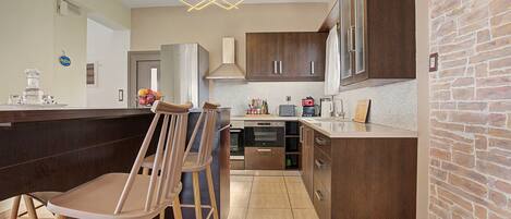 A modern kitchen with a central island, bar stools, a built-in oven, and a brick accent wall.