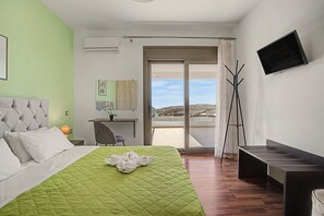 Habitación de hotel con cama, escritorio, silla, televisión y balcón con vistas.