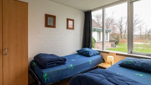 Ein Zimmer mit zwei Einzelbetten, einem Holzschrank und einem Fenster mit Blick auf ein Gebäude und Bäume.