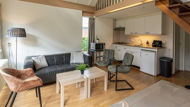 Ein modernes Interieur mit einer Couch, Sesseln, einem Tisch, einer Küchenzeile und einer Treppe.