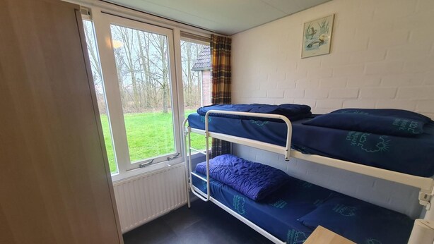 Una habitación tipo dormitorio con literas, un radiador, una ventana con cortinas e imagen en la pared.