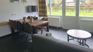 Un área de comedor con una mesa y sillas, un televisor montado en la pared y vistas al exterior a través de amplios ventanales.
