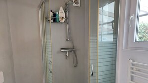 Ducha con puerta de cristal, cabezal de ducha de mano y grifo empotrado en la pared.