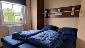 Un dormitorio con cama, ventana, radiador y estante con tazas.