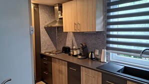 Una cocina moderna con armarios de madera oscura, una campana extractora de acero inoxidable, una estufa a gas, una cafetera y un ventanal con persianas.