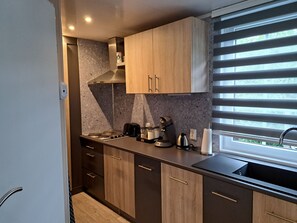 A modern kitchen with dark wood cabinets, a stainless steel range hood, a gas stove, a coffee maker, and a window with blinds. - RBR 1233 - Beach Resort Kamperland by Interhome (Kamperland)