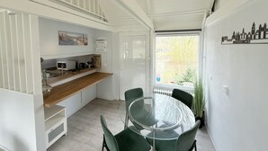 Une cuisine moderne avec des meubles blancs, un plan de travail en bois et un coin repas comprenant une table en verre et des chaises vertes.
