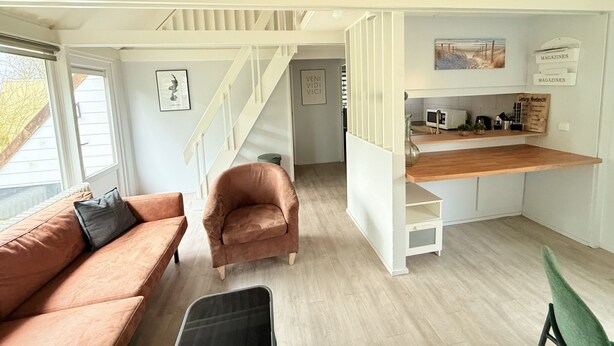 Un espace de vie compact comprenant un canapé, un fauteuil, un coin cuisine et un escalier.