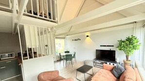 Un espace de vie moderne comprenant un escalier, un coin repas, un canapé, un téléviseur et une plante en pot.