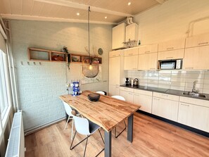 Eine moderne Küche mit Holztisch, weißen Stühlen, einer Hängeleuchte und einer eingebauten Mikrowelle.