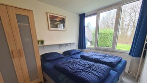 Una habitación con dos camas, un armario, una ventana con cortinas, un radiador y un cuadro en la pared.
