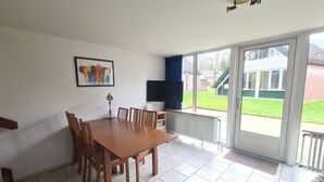 Un comedor con mesa y sillas, un televisor y vista a un césped verde a través de un ventanal corredero.