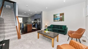 Una sala moderna con sofá, mesa de centro y sillas, una escalera y una cocina al fondo.