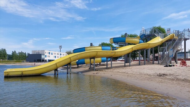Een waterglijbaanconstructie met meerdere glijbanen, een zandstrand en een gebouw op de achtergrond.