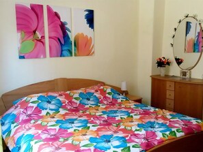 Ein Schlafzimmer mit floralem Bettbezug, einem Holzkopfteil, einem Schminktisch mit Spiegel und Wandbildern.