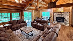 A log cabin interior with a fireplace, wooden furniture, and large windows.