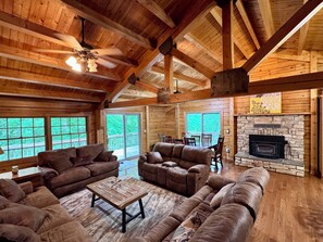 A log cabin interior with a fireplace, wooden furniture, and large windows. - Cozy Waterfront Log Cabin Retreat on a Quiet Creek (Mineral)